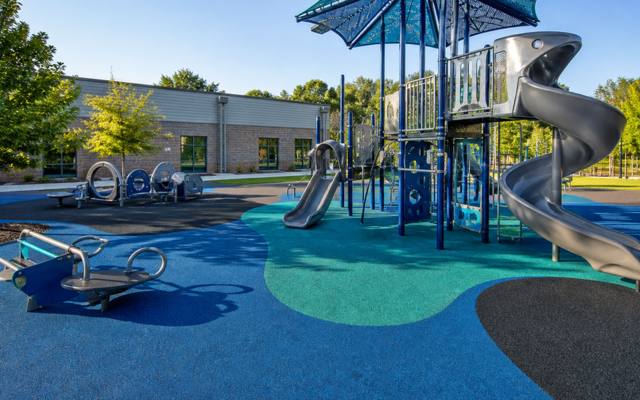 Playground with a spiral slide standing on blue and green rubber safety surfacing.
